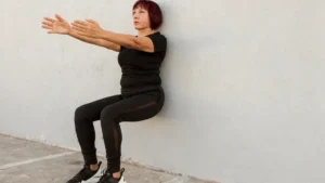 Mature woman performs a steady wall sit to build muscle and support functional independence.