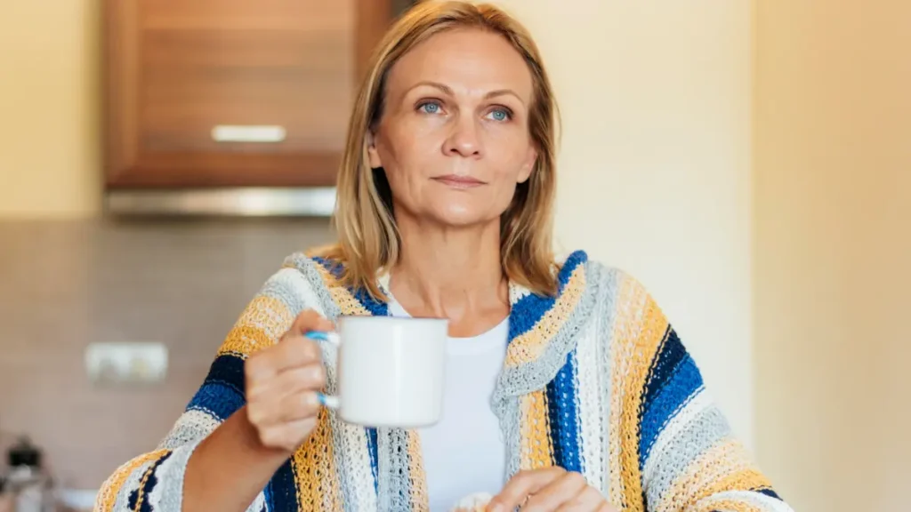 Mature woman thoughtfully holding a warm coffee mug while managing metabolic heat production during her morning routine.