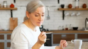 Mature woman checking a thermometer at her kitchen table to investigate frequent colds and a sluggish immune response.