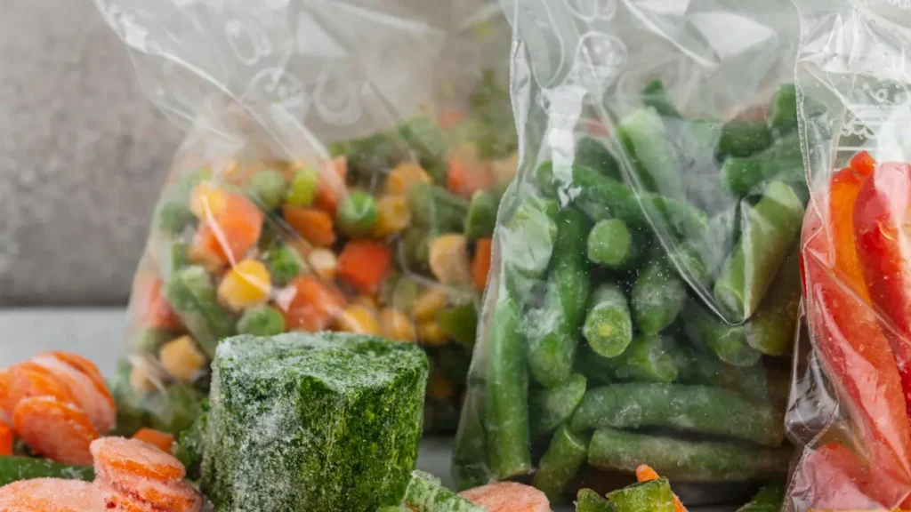 Various clear bags of frozen mixed vegetables, green beans, and peppers alongside a frozen block of chopped spinach.