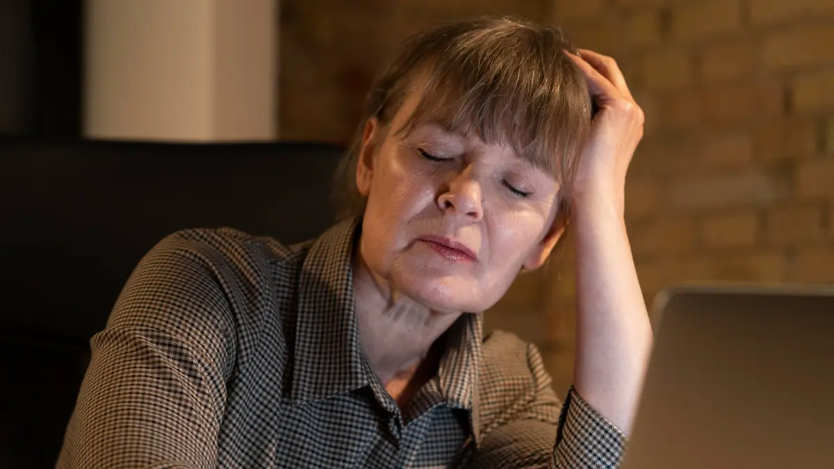 Mature woman feeling a 4pm energy crash at her desk, showing fatigue linked to meal timing and metabolism.