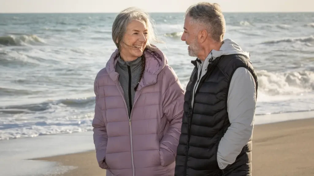 Active mature couple walking briskly on a beach to support basal metabolic rate and cognitive health.