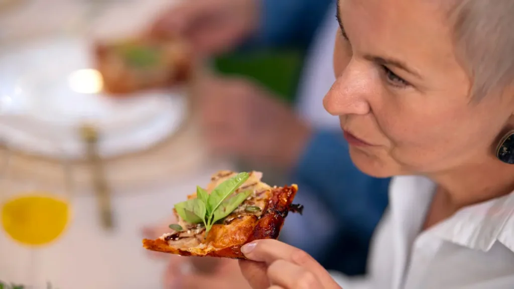 Woman pausing mindfully before eating a bite of food at a dinner table, practicing slow and intentional eating habits.