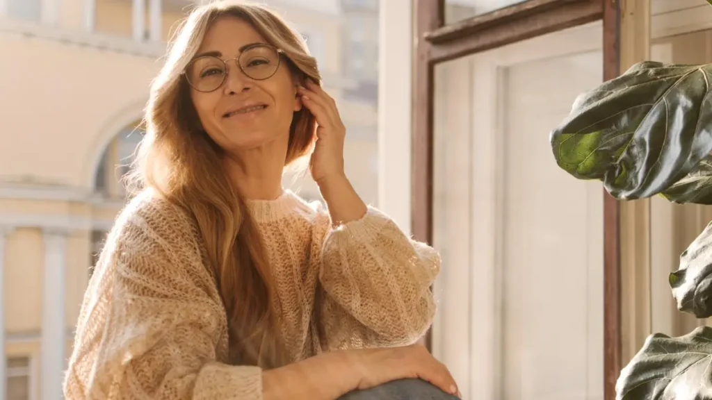 Mature woman sitting by a sunlit window to stimulate metabolic heat production and reset her internal clock