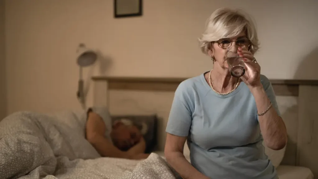 "Mature woman drinking water at 3 AM to manage a metabolic wake-up and cortisol-induced thirst.