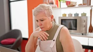 Mature woman reflecting on gut inflammation signs after 50 while pausing in her kitchen.