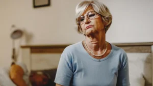 Mature woman sitting on edge of bed to manage orthostatic hypotension after 50.