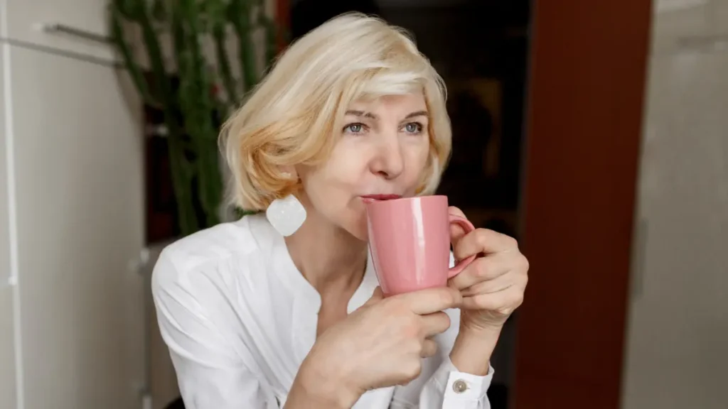 Mature woman sipping from a mug to mask a hormonal crash and blunting her natural cortisol management.