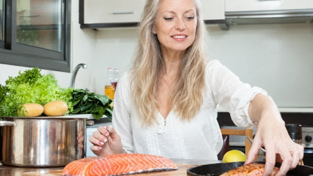 Woman in her 50s preparing salmon in a kitchen, one of the few foods with meaningful vitamin D content.
