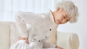 Woman in her 50s pressing hand to hip at dawn, experiencing bone aches linked to vitamin D3 vs D2 absorption.
