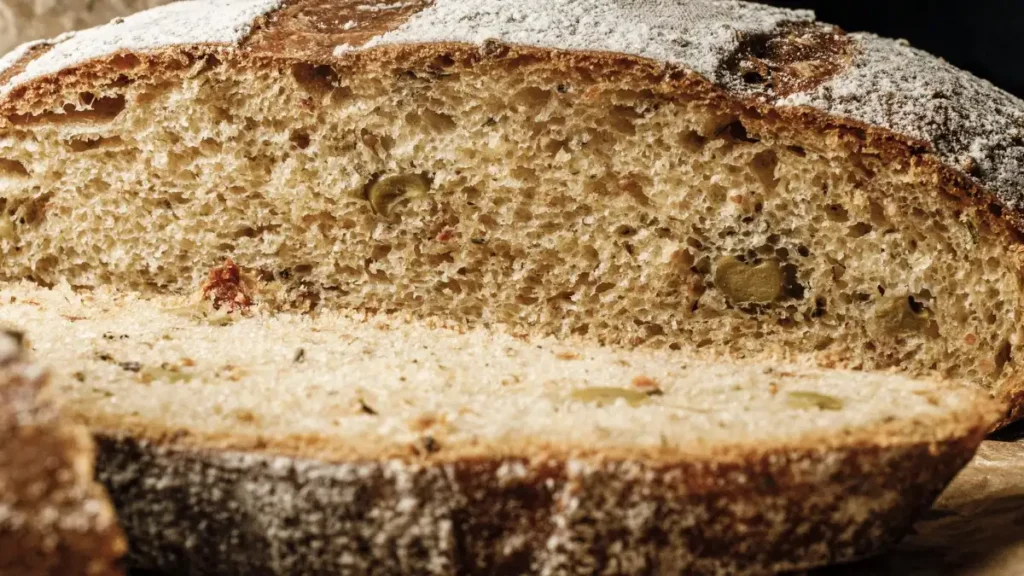 A sliced artisan no-knead bread loaf with a flour-dusted crust and airy crumb structure.