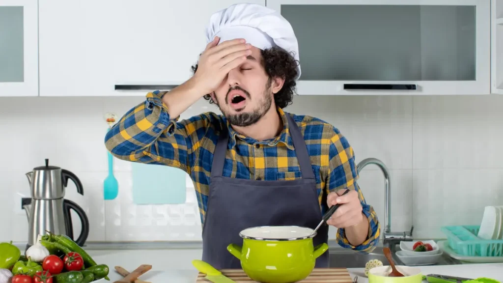 A man in a chef's hat and apron looking frustrated over a pot of food, illustrating the moment of realization when a recipe goes wrong.