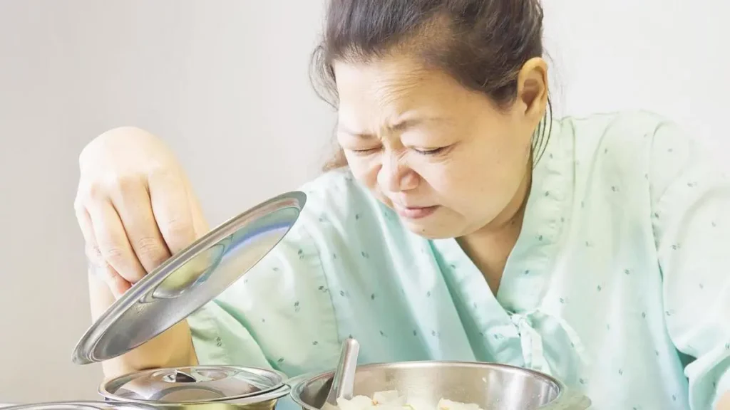 Mature Asian woman pulling away from her plate and grimacing due to nausea from insulin resistance after menopause.