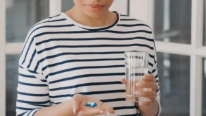 Woman holding a handful of capsules and water while considering vitamins for over 50 and supplement absorption.