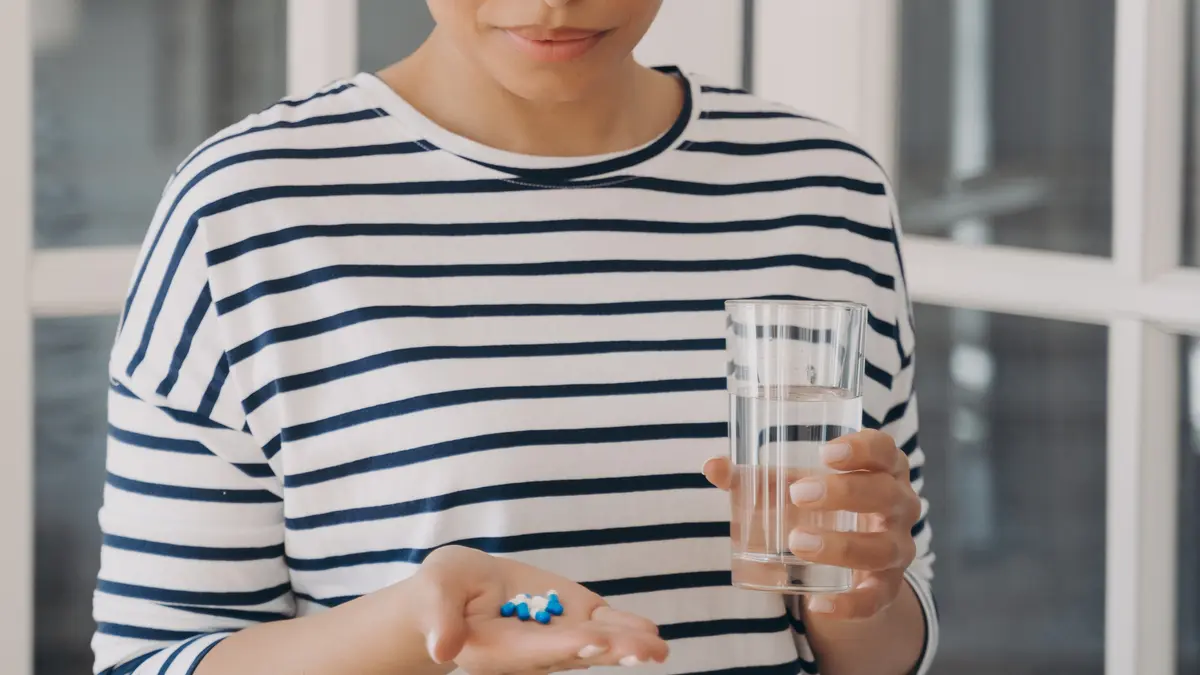 Woman holding a handful of capsules and water while considering vitamins for over 50 and supplement absorption.