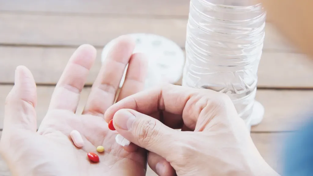 Woman holding a handful of capsules and water while considering vitamins for over 50 and supplement absorption.