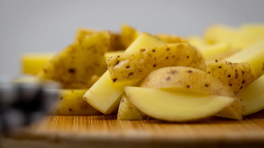 Thinly sliced raw potatoes on a worn wooden board, conserving beneficial resistant starch to support basal metabolic rate.