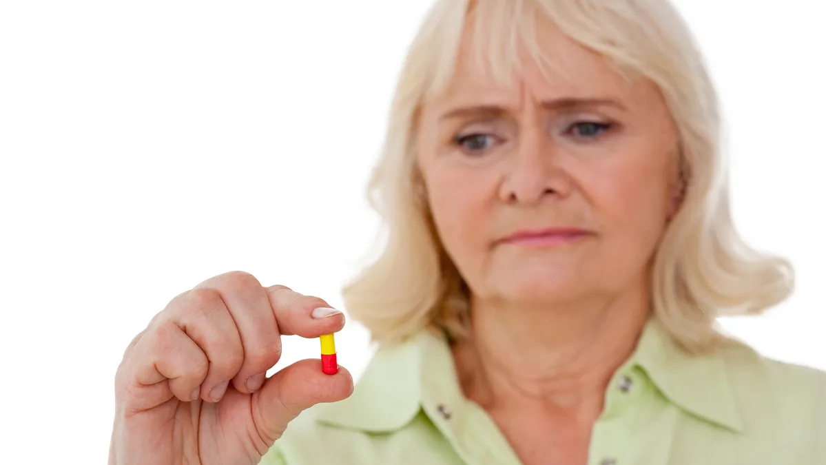 A woman over 50 holds a single supplement capsule with a doubtful expression, questioning whether her vitamins are actually working.