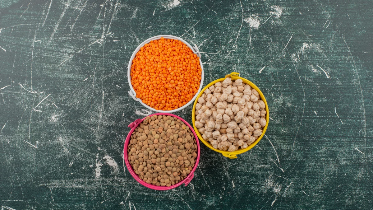 Three colorful buckets filled with raw red lentils, brown lentils, and chickpeas highlighting nutrient-dense foods for maintaining muscle and longevity after 50.
