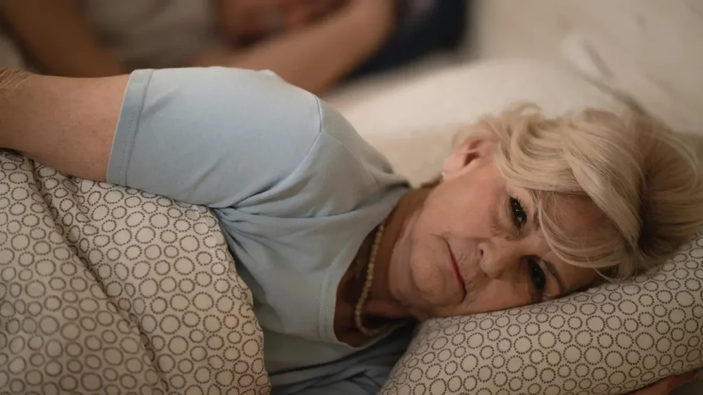 Mature woman lying awake in bed with a racing mind caused by slow autonomic recovery and low vagal tone.