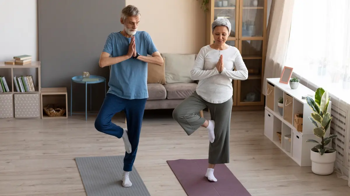Senior couple practicing Tree Pose at home on mats to improve postural stability and pass the balance test after 50.