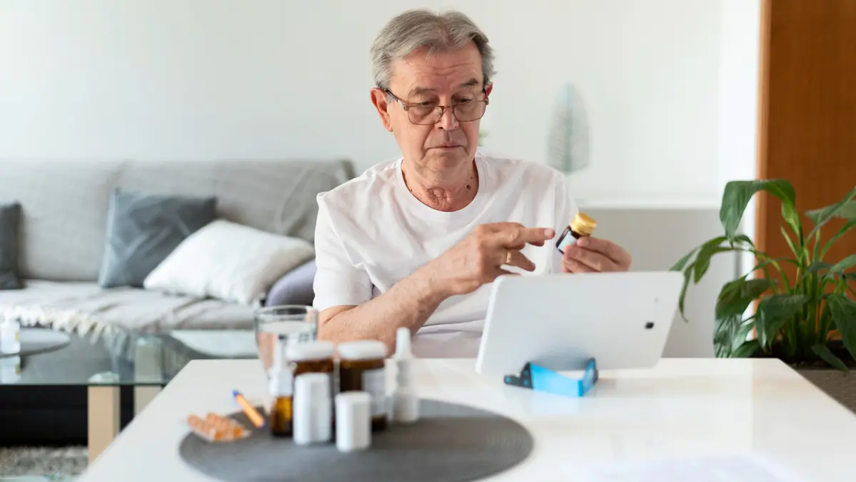 Mature man in living room reviewing Omega 3 Index Test results on a laptop with supplements placed near him on the table.