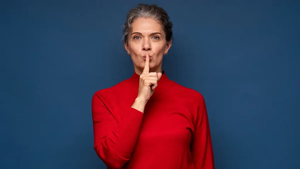 Mature woman signaling for silence to focus on deep nasal breathing and trigger the parasympathetic rest response.