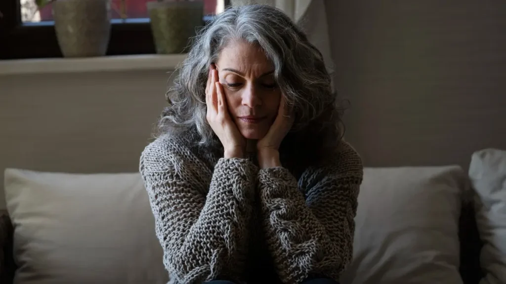 Mature woman with silver hair holding her face in frustration while feeling the effects of daily cortisol management and stress.