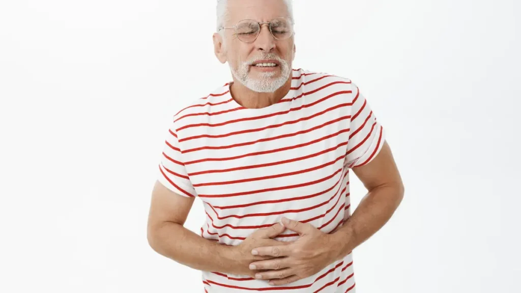 Mature man in a striped shirt clutching his stomach in discomfort to illustrate age-related bloating and reduced basal metabolic rate.