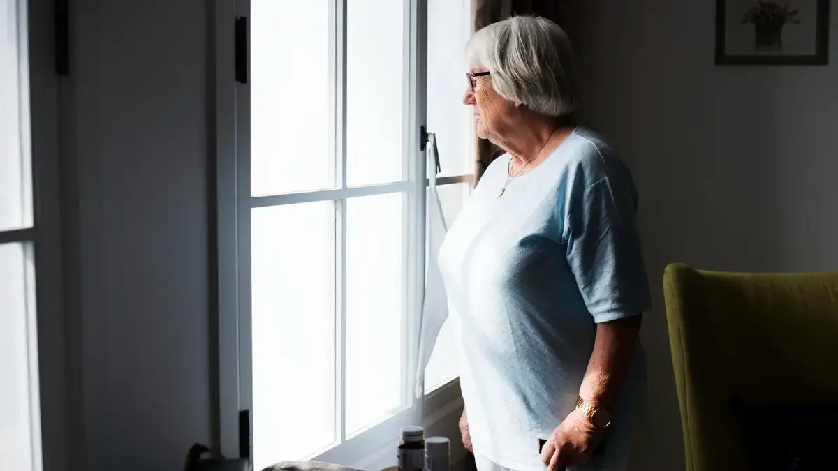 Mature woman looking out a window with a pensive expression while practicing cortisol management to lower daily stress levels.