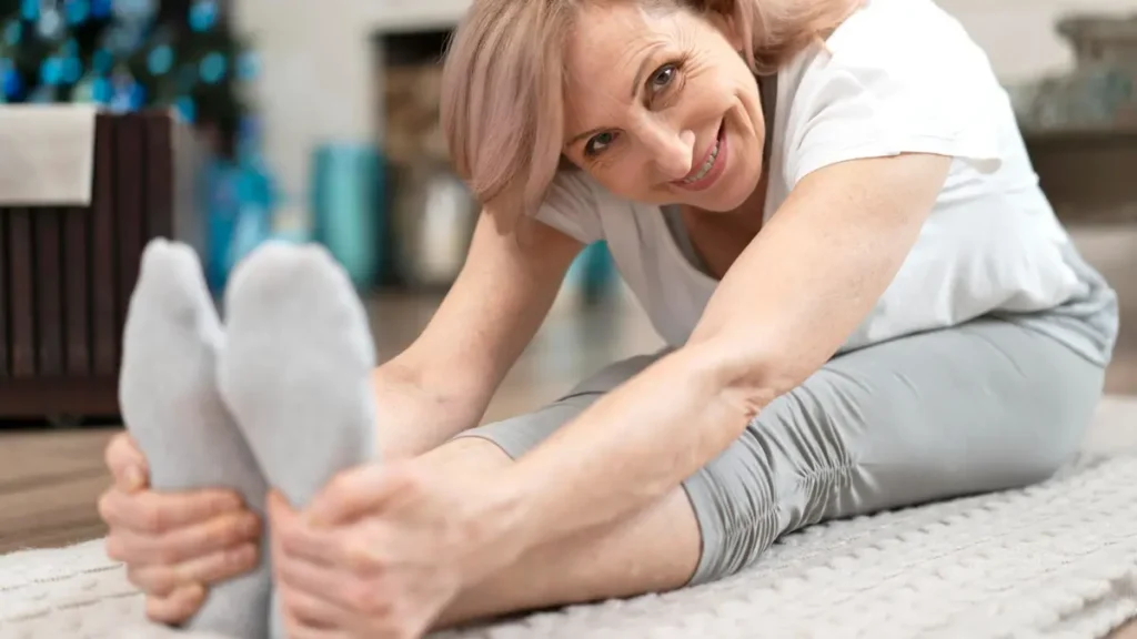 Mature woman smiling while performing seated flexibility stretches at home to improve the neural plasticity required for the balance test after 50.