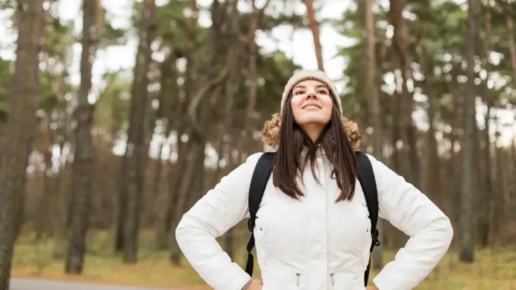 Young woman standing in a forest with an open chest and upright posture to demonstrate deep breathing in nature.