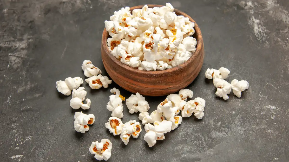 Healthy whole grain snack featuring a bowl of plain air-popped popcorn on a rustic dark background.