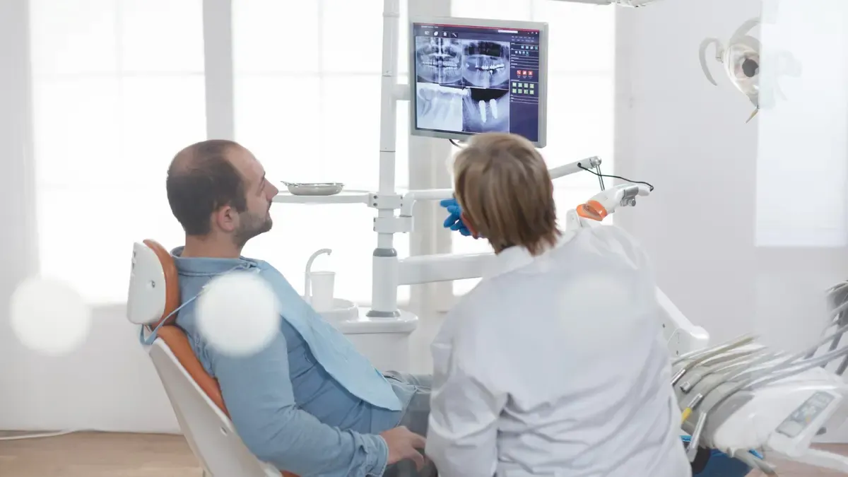 A dentist reviews digital dental X-rays on a monitor with a patient in a bright, modern office, illustrating the importance of requesting a professional periodontal screening for gum health.