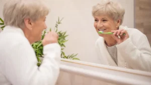 Mature woman looking at her reflection during morning dental care to manage periodontal disease heart risk.