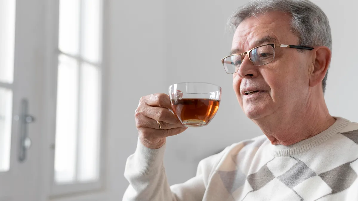 Mature man in glasses holding a clear glass of tea while considering the common green tea weight loss mistakes related to morning stomach acidity.