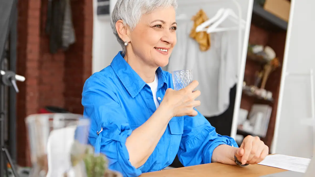  Mature woman drinks a refreshing glass of water at her desk to support fiber digestion and prevent afternoon fatigue.
