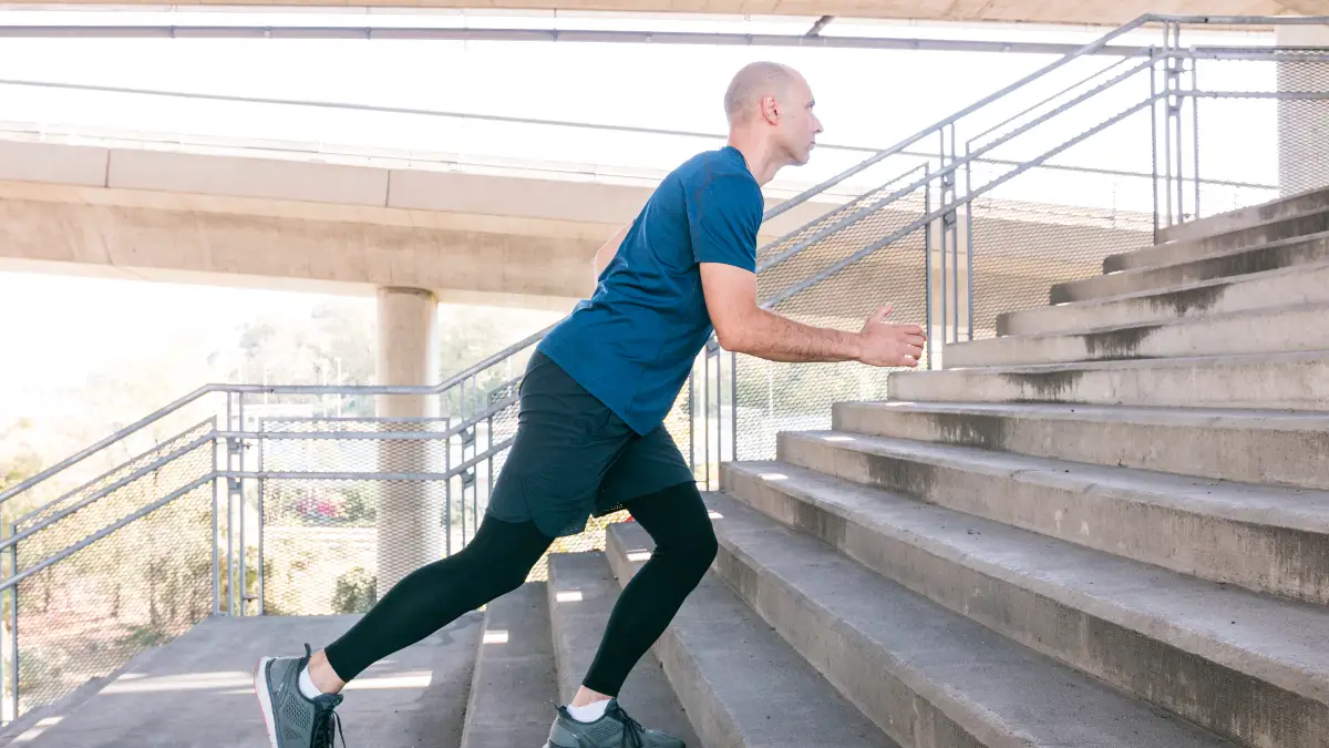 Male athlete performing a step-up on a concrete staircase, showing the leading foot flat on the step and the knee tracking forward to maintain joint alignment.