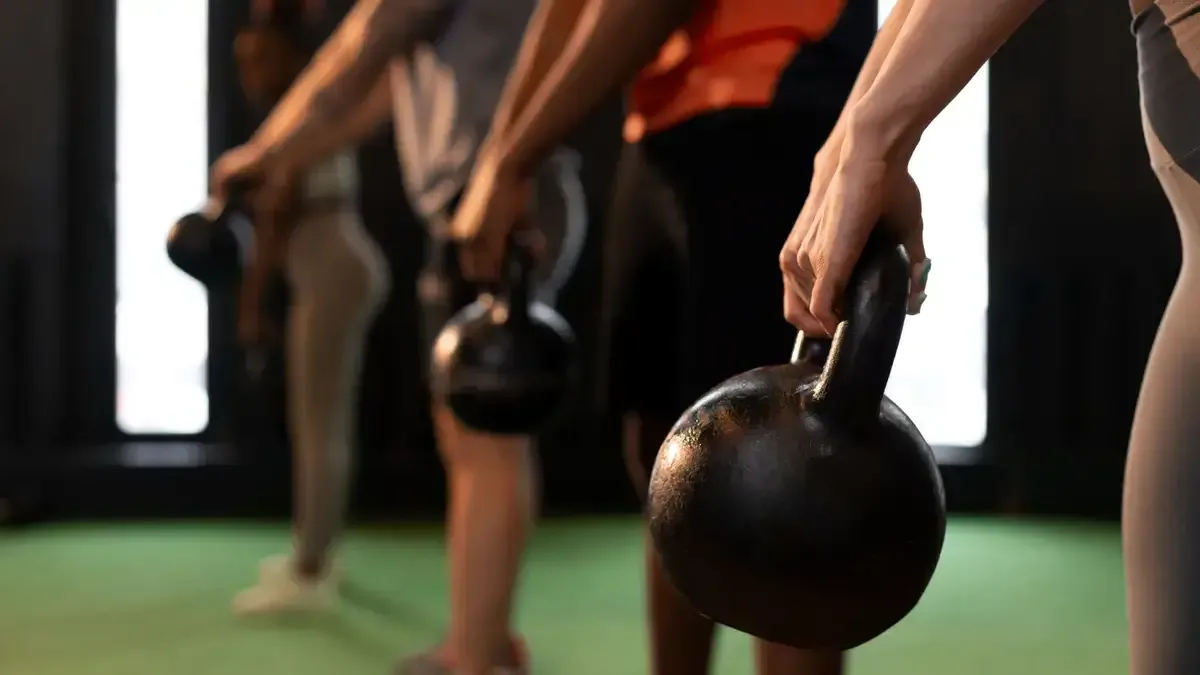 Close-up of diverse hands firmly gripping heavy kettlebells to build the functional grip strength necessary for metabolic longevity and fall prevention.
