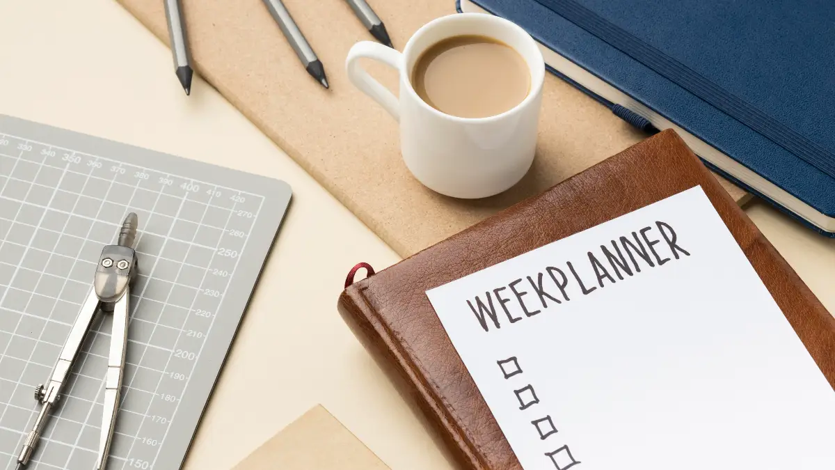 Flat lay of a desk featuring a leather notebook with a "Week Planner" checklist, a cup of coffee, and drafting tools used to organize a consistent VMO strengthening routine.