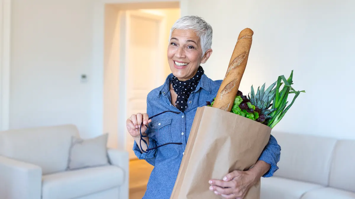 Mature woman holding a bag of fresh groceries to illustrate the functional strength and energy gains from consistent protein timing.