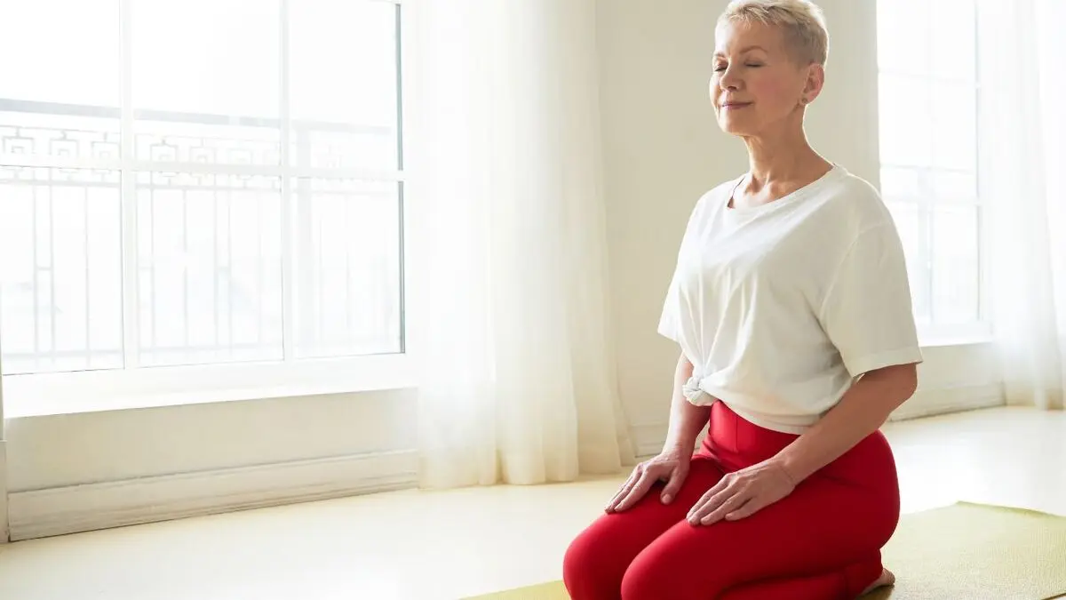 Mature woman practicing tall postural elongation and diaphragmatic breathing to manage intra-abdominal pressure and support holistic pelvic floor health.