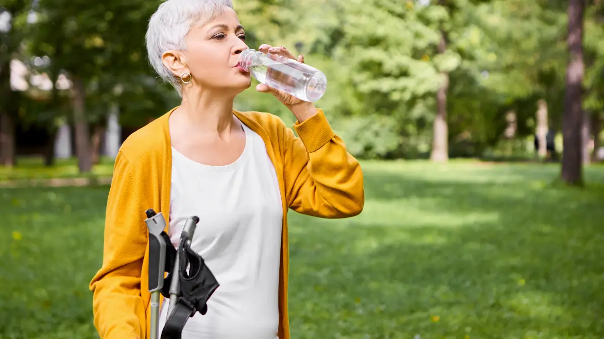 Active mature woman with Nordic walking sticks drinking water to maintain metabolic heat production and prevent sodium-related mineral swings that cause leg cramps.
