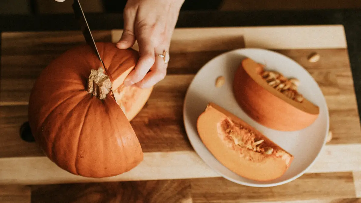 Hands slicing a fresh pumpkin on a wooden board to harvest zinc-rich seeds for supporting microscopic muscle repair and tissue recovery.