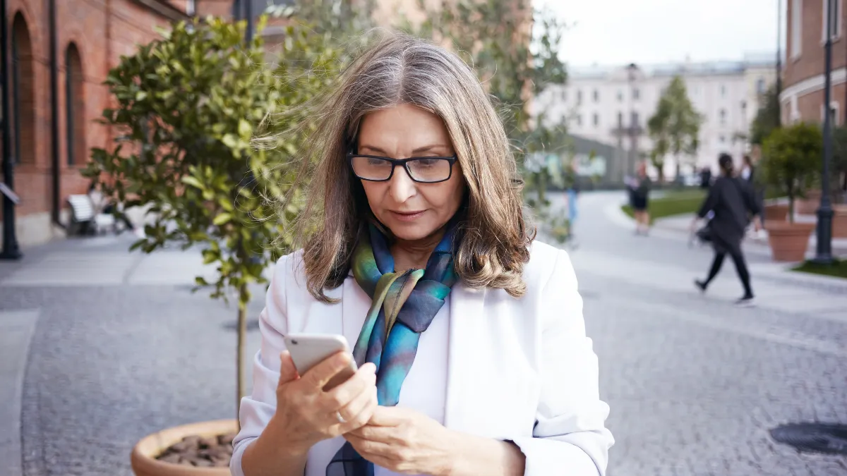 Mature woman looking down at phone while walking to illustrate how poor neck alignment affects hypothyroidism after 50.