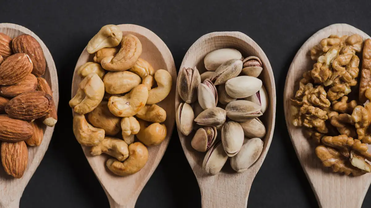 Four wooden spoons displaying raw almonds, cashews, pistachios, and walnuts representing the simple daily snack habit linked to a lower risk of cardiovascular disease after 50.