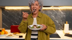 Vibrant mature woman enjoying a fresh fig and mixed greens salad in her kitchen to maintain a high fiber diet after 50.