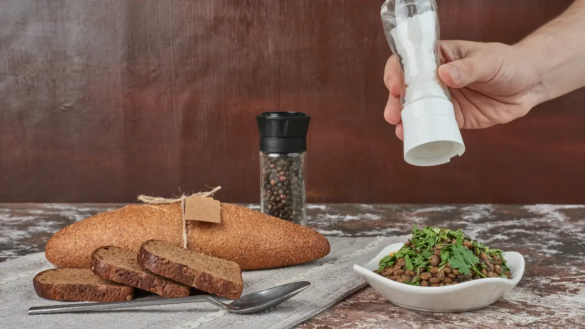 Hand adding salt to a meal, a common habit that can lead to sodium-related calcium loss in the kidneys