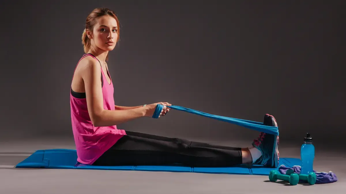 Woman in a pink tank top performing a seated row with a blue resistance band to load the upper spine and protect the vertebrae from bone loss