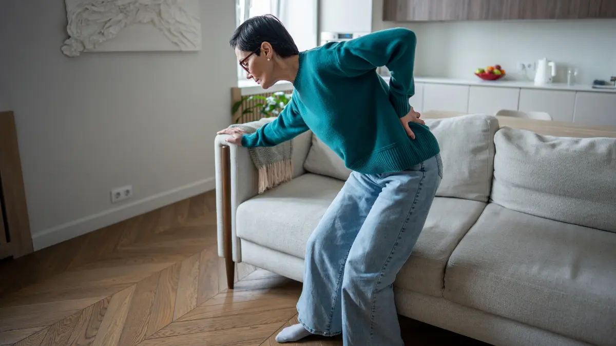 Mature women wincing while rising from a chair to illustrate psoas-related stiffness during spinal extension